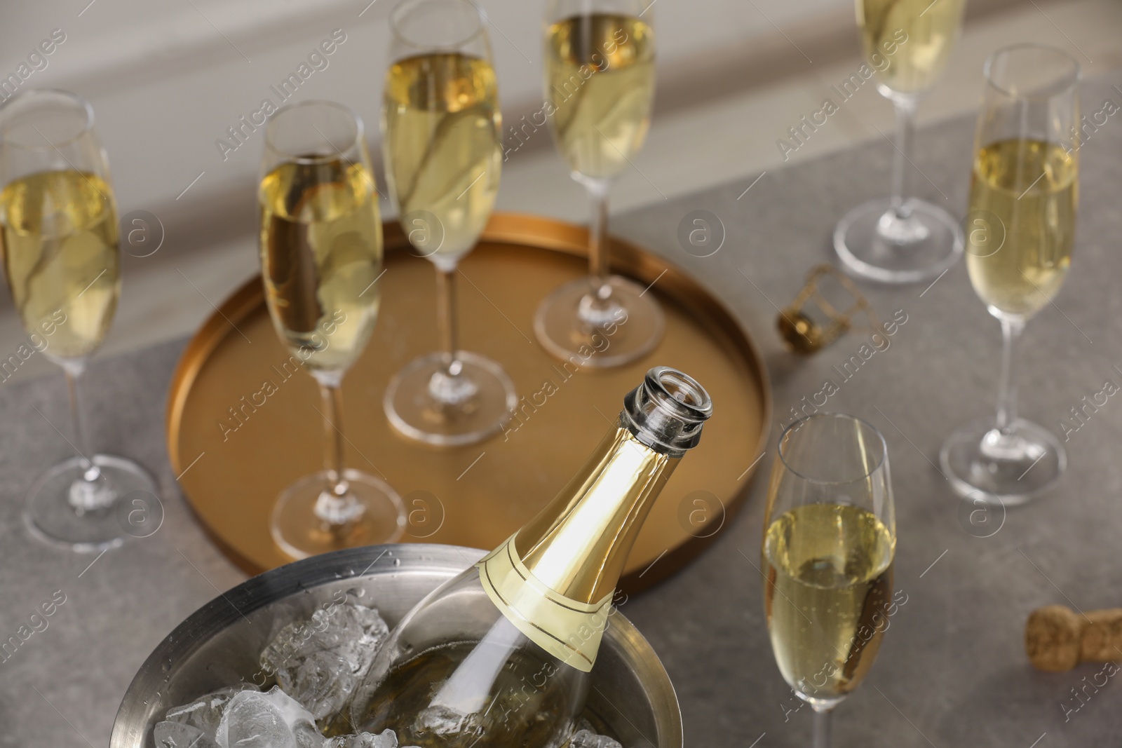 Photo of Bottle of sparkling wine in cooler bucket and glasses on grey table, closeup