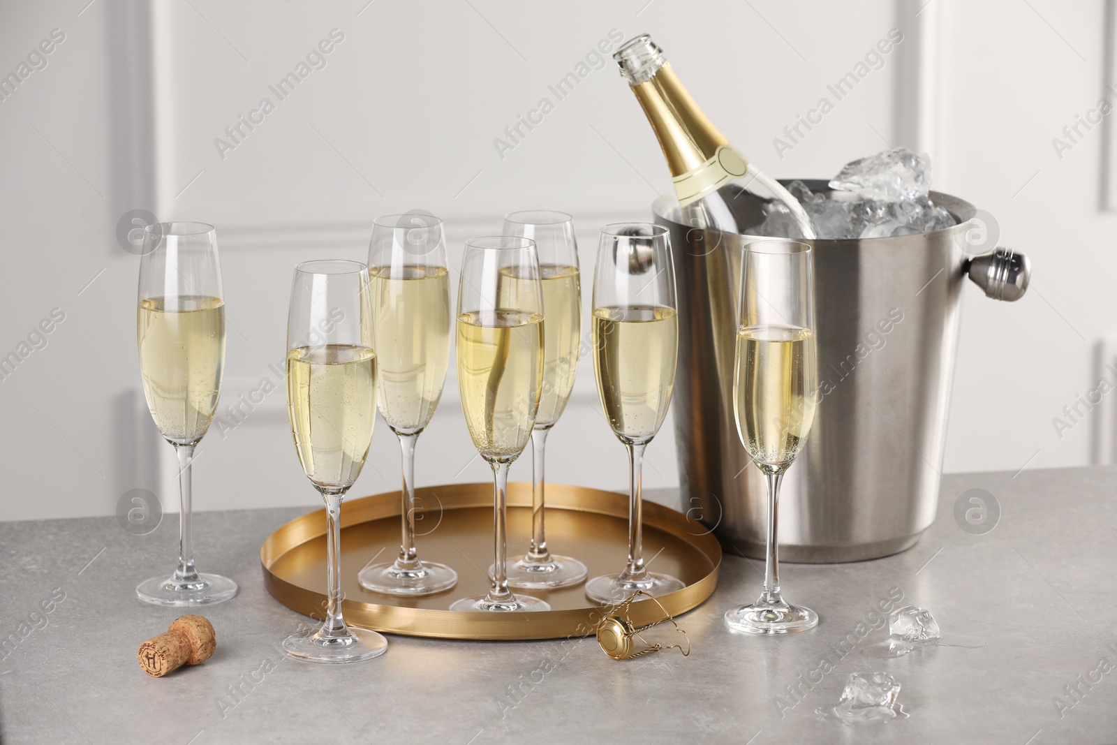 Photo of Bottle of sparkling wine in cooler bucket and glasses on grey table