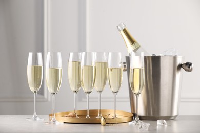 Photo of Bottle of sparkling wine in cooler bucket and glasses on grey table