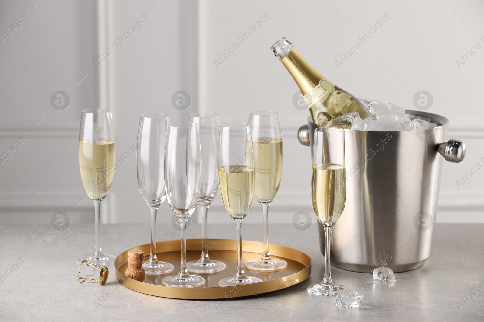 Photo of Bottle of sparkling wine in cooler bucket and glasses on light table