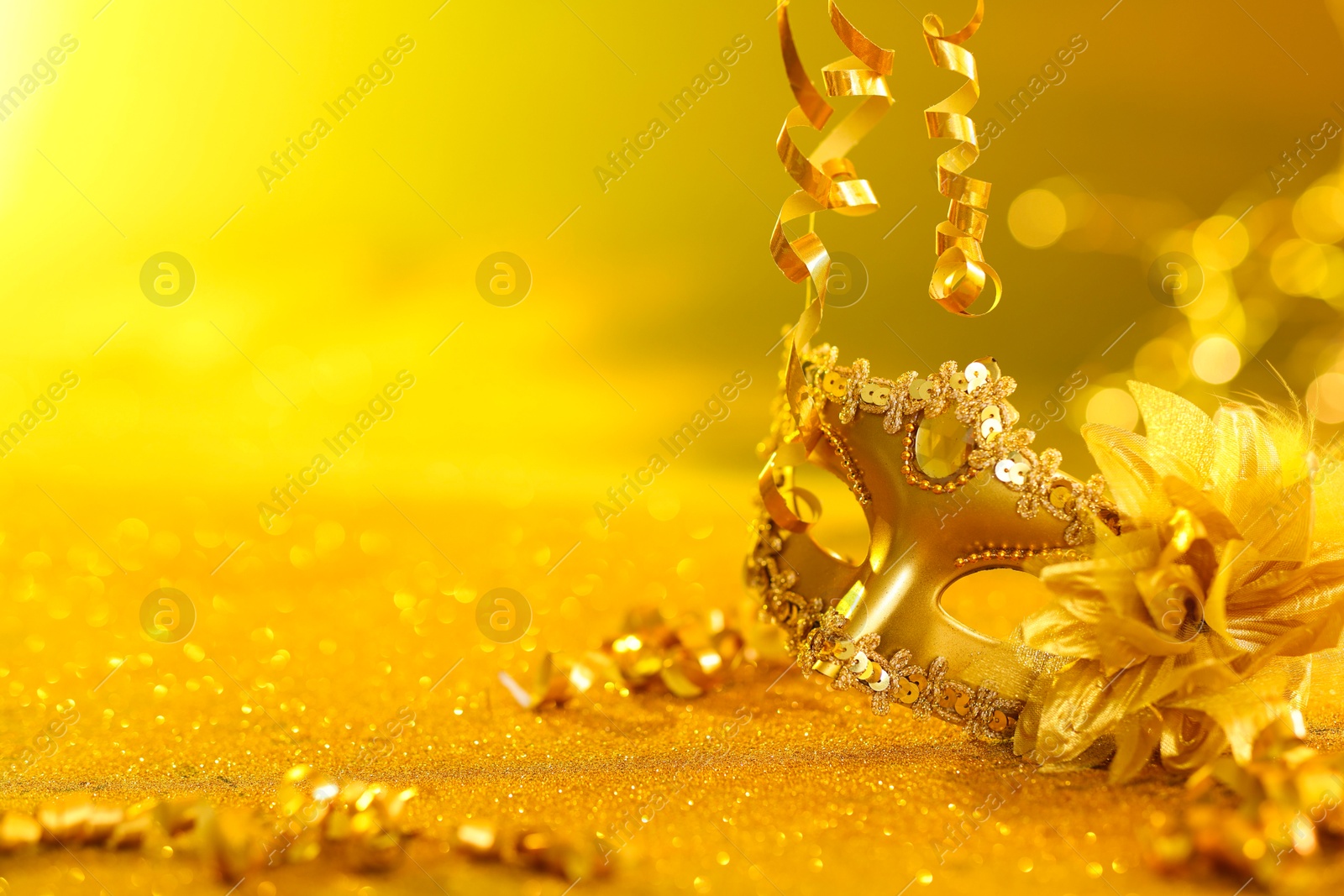 Photo of Beautiful carnival mask on golden shiny surface, closeup. Space for text