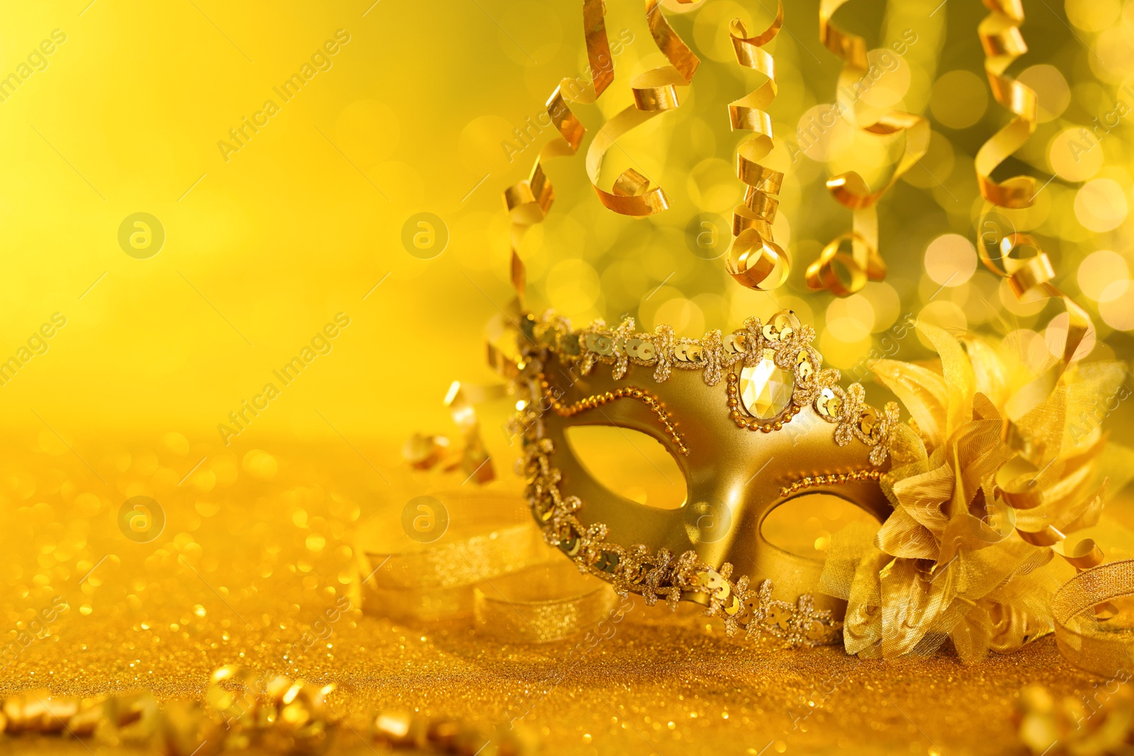 Photo of Beautiful carnival mask on golden shiny surface, closeup. Space for text