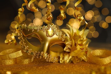 Photo of Beautiful carnival mask on golden shiny surface against blurred lights, closeup