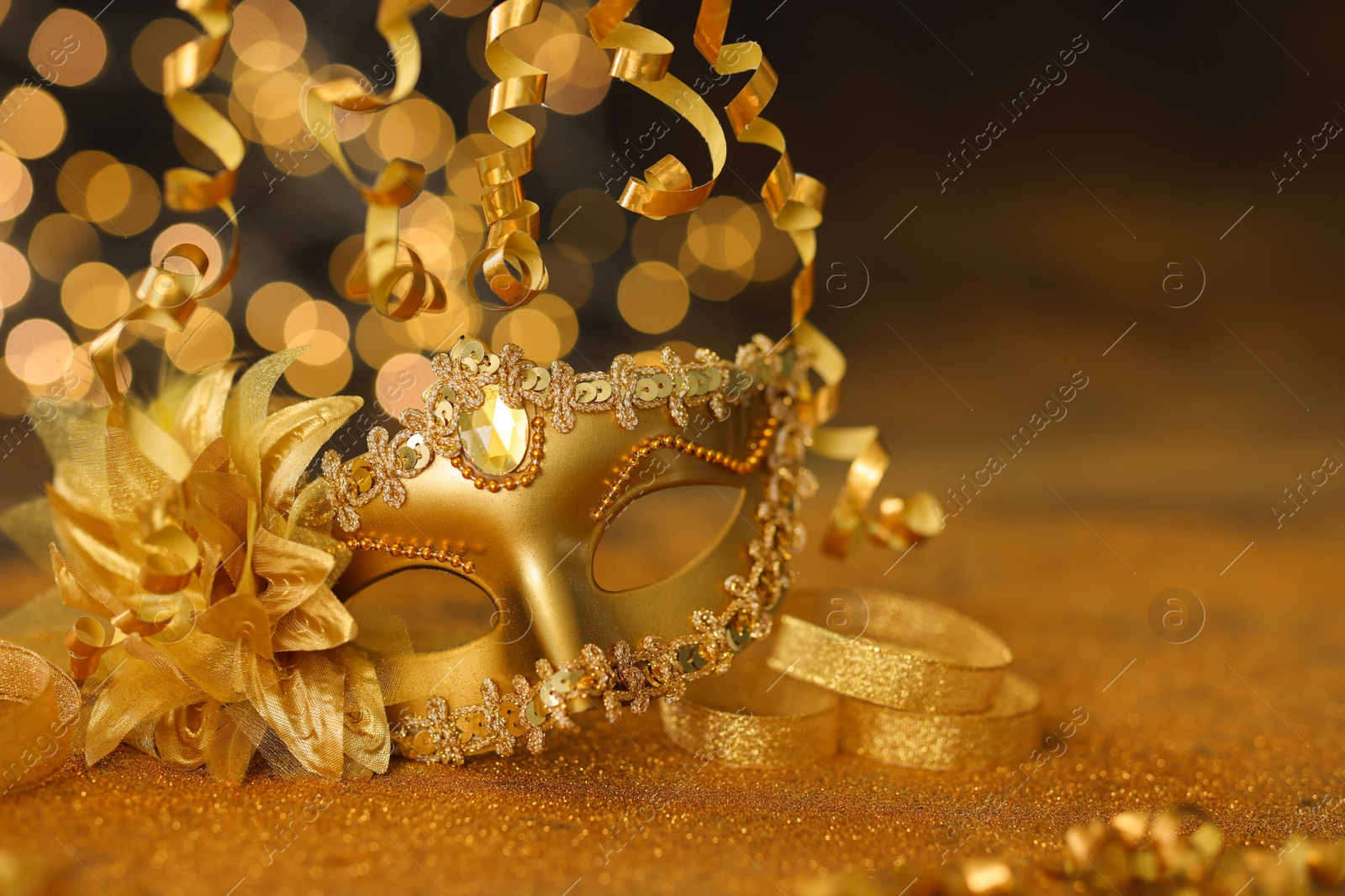 Photo of Beautiful carnival mask on golden shiny surface, closeup. Space for text