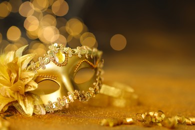 Photo of Beautiful carnival mask on golden shiny surface, closeup. Space for text