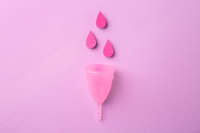 Photo of Menstrual cup and paper cutouts of drops on violet background, flat lay