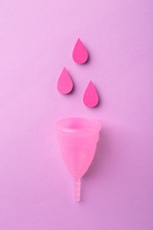 Photo of Menstrual cup and paper cutouts of drops on violet background, flat lay