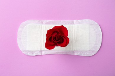 Photo of Menstrual pad with red flower on violet background, top view