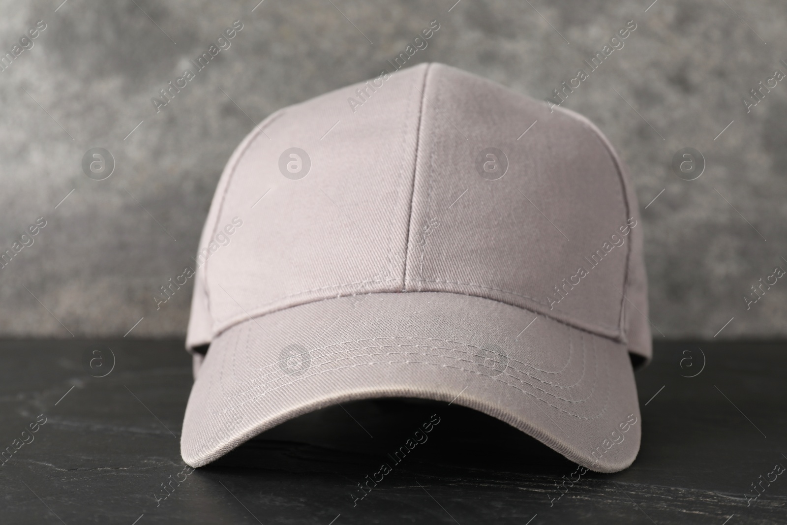 Photo of Stylish baseball cap on dark textured table, closeup. Mockup for design