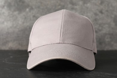 Photo of Stylish baseball cap on dark textured table, closeup. Mockup for design