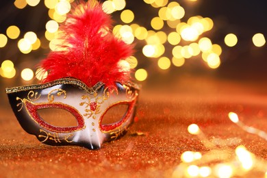 Photo of Beautiful carnival mask on shiny color background, bokeh effect. Space for text