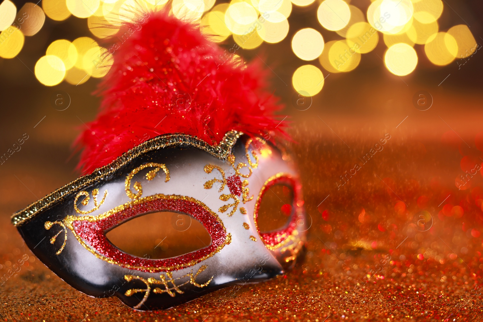 Photo of Beautiful carnival mask on shiny color background, closeup. Bokeh effect