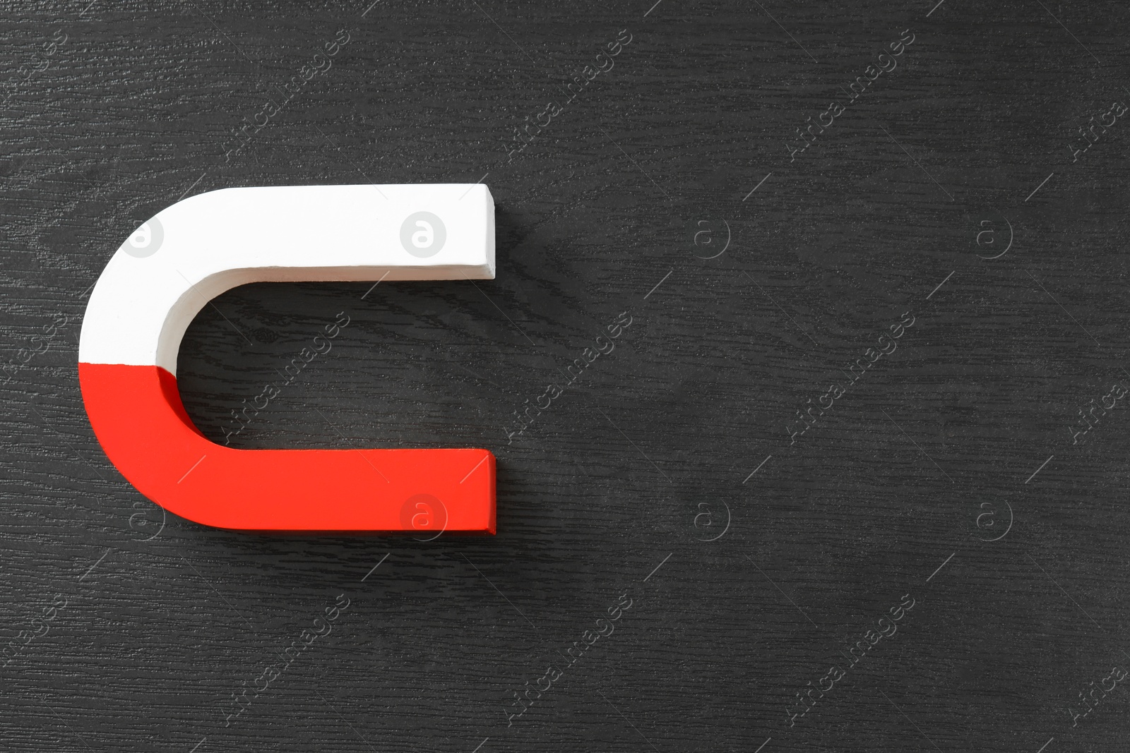 Photo of One horseshoe magnet on black wooden background, top view. Space for text