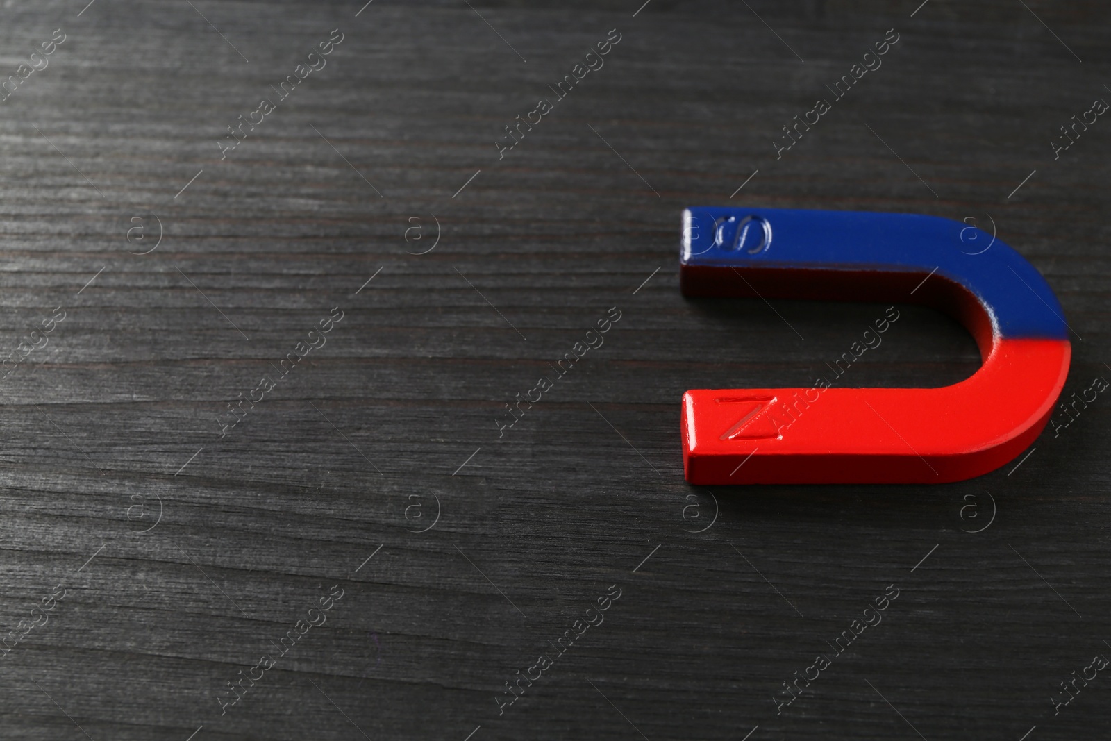 Photo of One horseshoe magnet on black wooden table, space for text