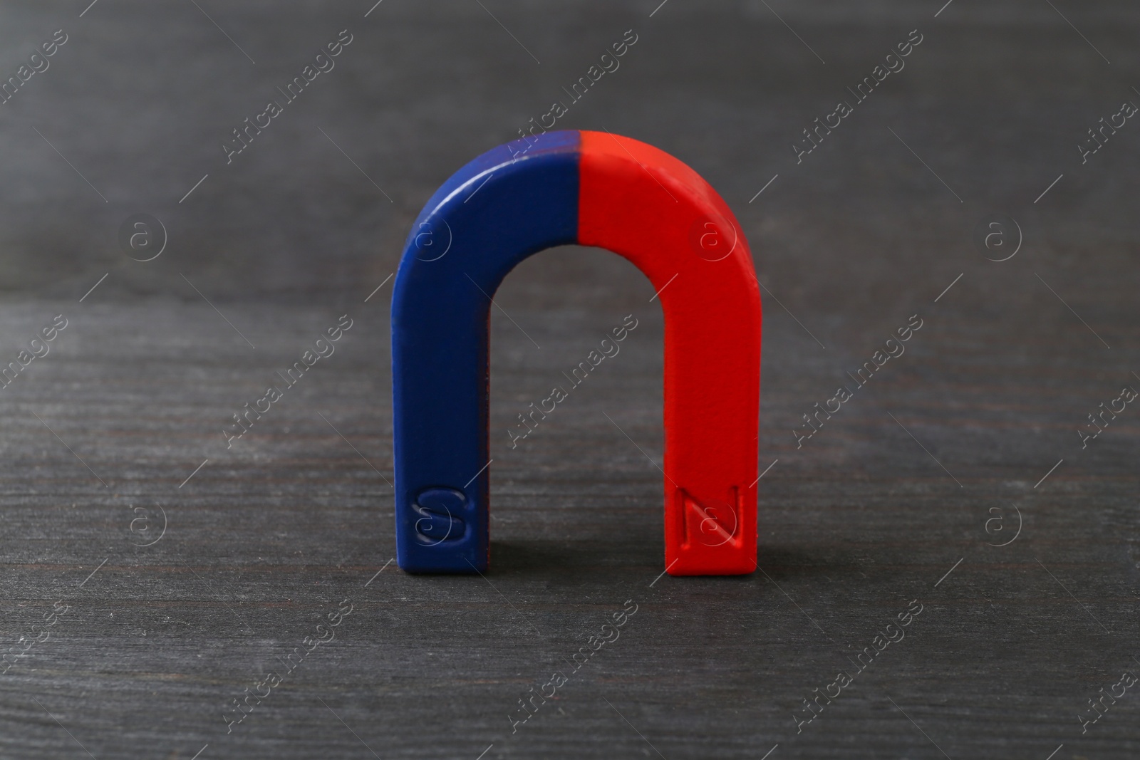 Photo of One horseshoe magnet on black wooden table, closeup