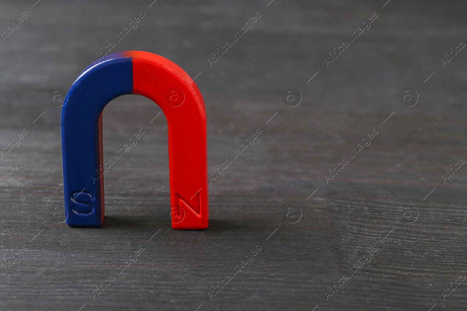 Photo of One horseshoe magnet on black wooden table, space for text