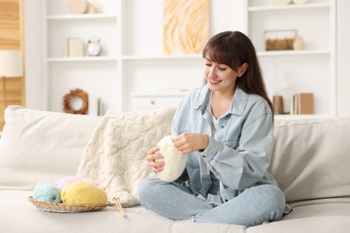 Photo of Beautiful woman with colorful yarns and knitting needles on sofa at home