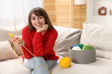 Photo of Beautiful woman with colorful yarns and knitting needles on sofa at home