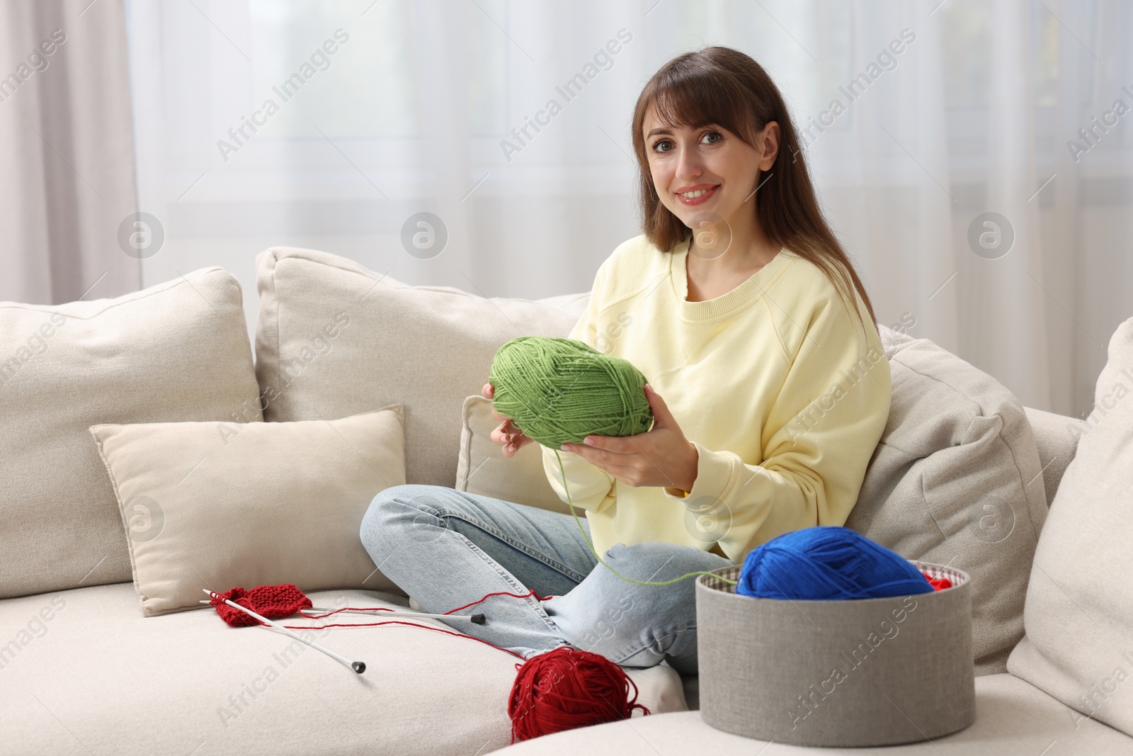 Photo of Beautiful woman with colorful yarns and knitting needles on sofa at home