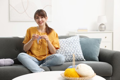 Photo of Beautiful woman crocheting with hook on sofa at home