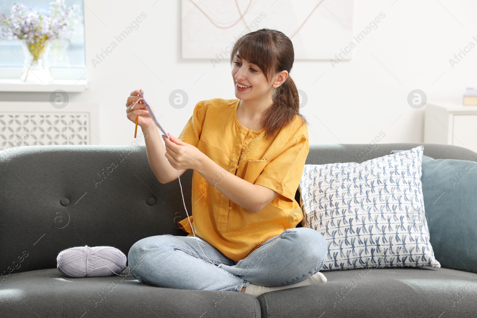 Photo of Beautiful woman crocheting with hook on sofa at home