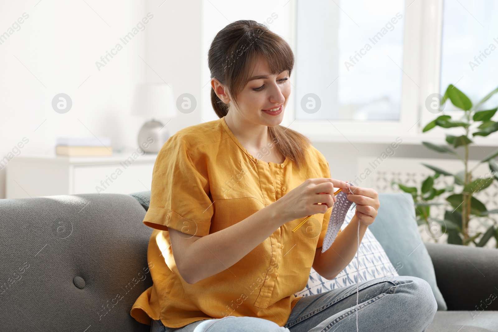 Photo of Beautiful woman crocheting with hook on sofa at home