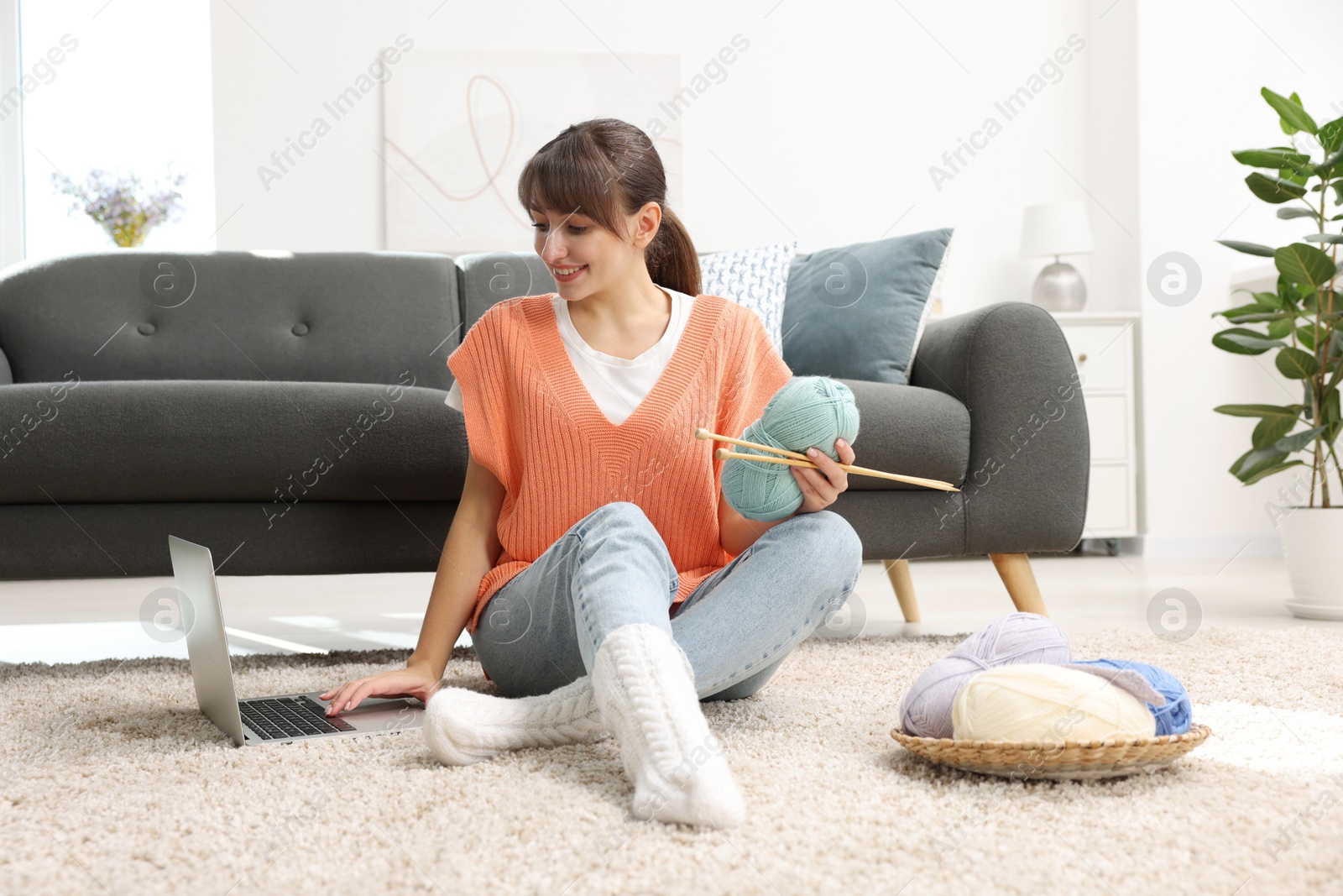 Photo of Beautiful woman learning to knit with online course on floor at home