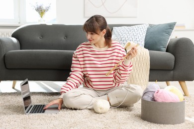 Photo of Beautiful woman learning to knit with online course on floor at home