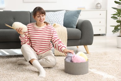 Beautiful woman with colorful yarns and knitting needles on floor at home