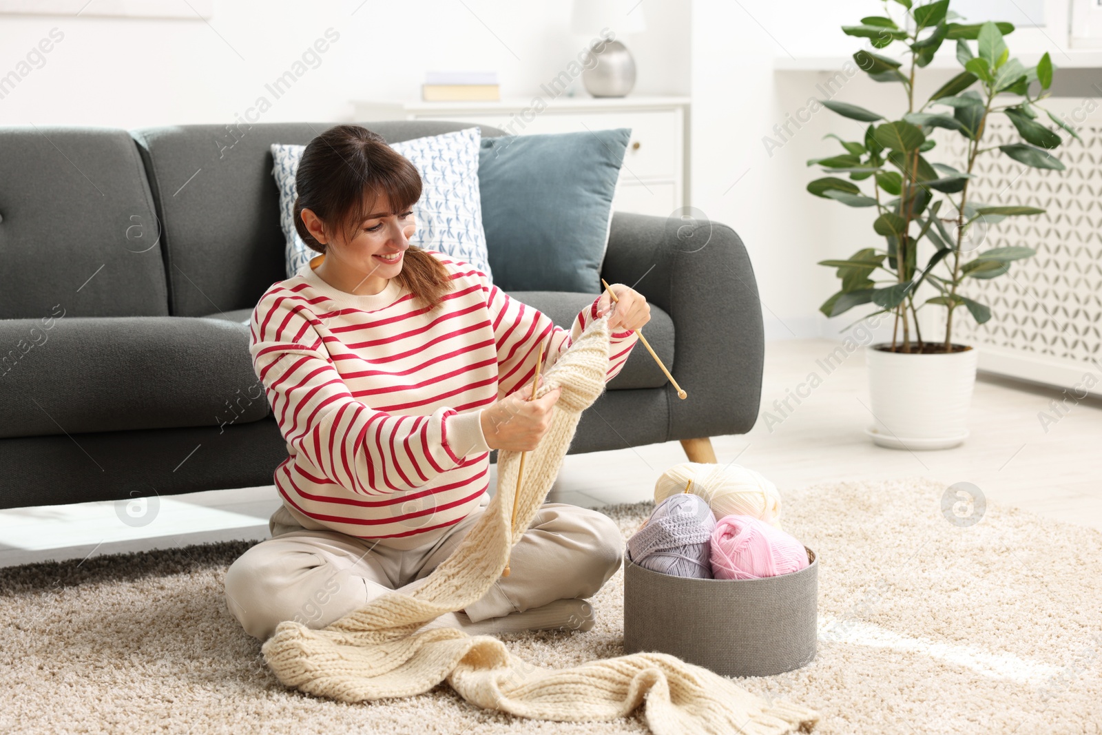 Photo of Beautiful woman knitting with needles on floor at home