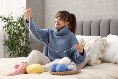 Photo of Beautiful woman with colorful yarns on bed at home. Knitting material