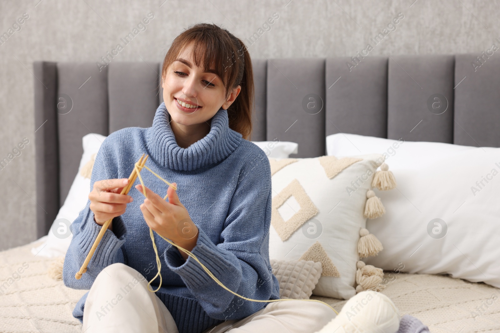 Photo of Beautiful woman knitting with needles on bed at home