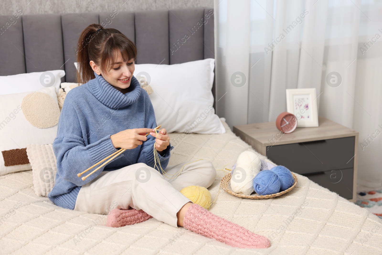 Photo of Beautiful woman knitting with needles on bed at home