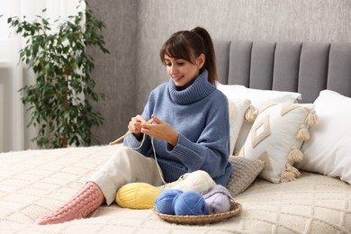 Beautiful woman knitting with needles on bed at home