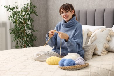 Beautiful woman knitting with needles on bed at home