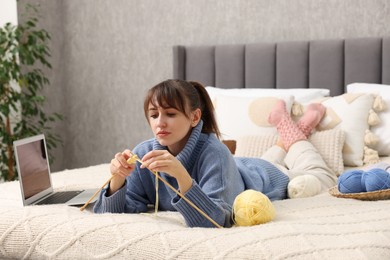 Woman learning to knit with online course on bed at home