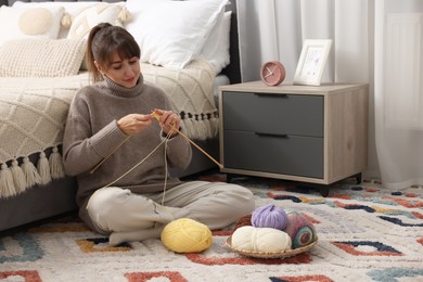 Beautiful woman knitting with needles on floor at home