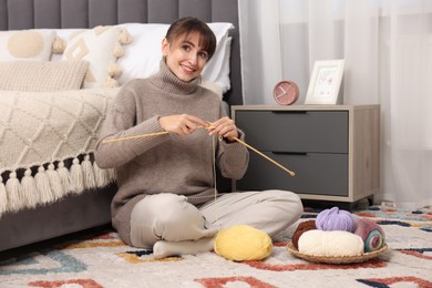 Beautiful woman knitting with needles on floor at home