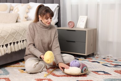 Beautiful woman with colorful yarns and knitting needles on floor at home