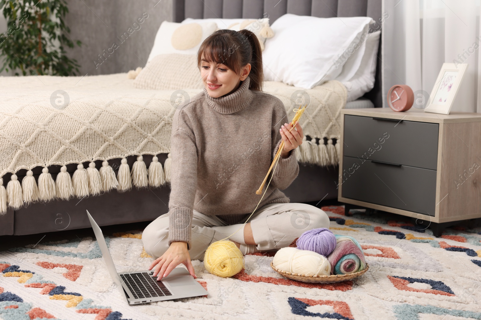 Photo of Woman learning to knit with online course on floor at home