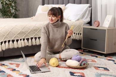 Woman learning to knit with online course on floor at home