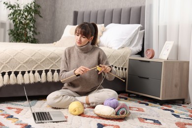 Photo of Woman learning to knit with online course on floor at home