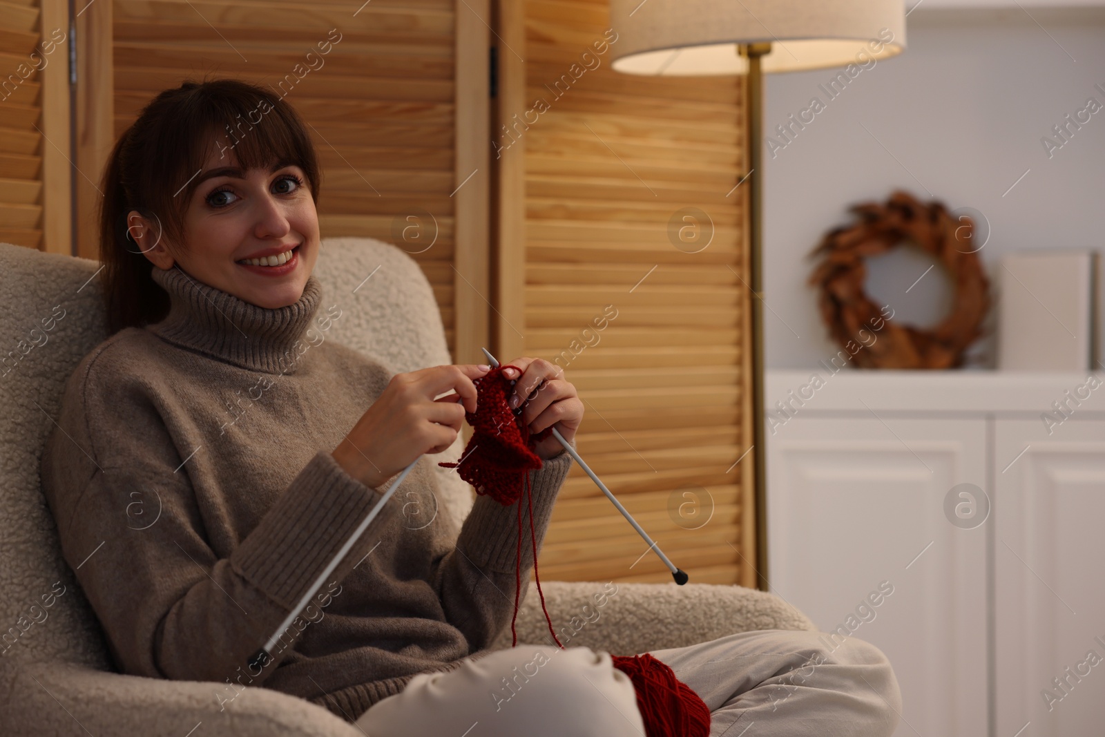 Photo of Beautiful woman knitting with needles in armchair at home