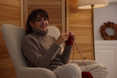 Photo of Beautiful woman knitting with needles in armchair at home