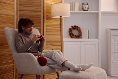 Beautiful woman knitting with needles in armchair at home