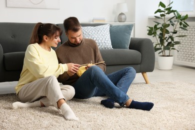 Photo of Woman teaching her boyfriend how to knit on floor at home