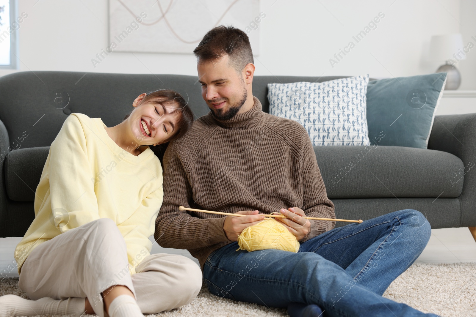 Photo of Woman teaching her boyfriend how to knit on floor at home