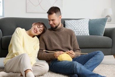 Woman teaching her boyfriend how to knit on floor at home