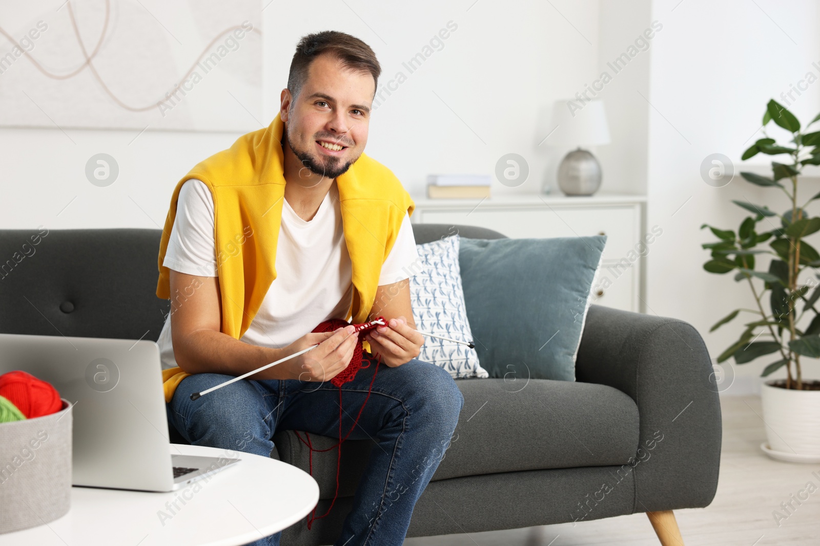 Photo of Man learning to knit with online course on sofa at home