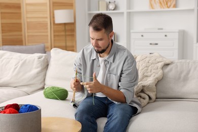 Man knitting with needles on sofa at home